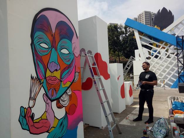 Seorang seniman saat membuat mural bertema badminton.